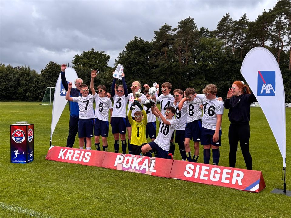 Jugendmannschaft in weißen Trikots jubelt mit Pokal am Banner „Kreispokalsieger“